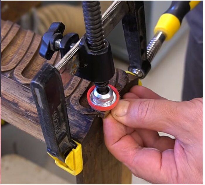 En tving med ett verktyg fäst i mitten, innehållande ett svart vred och en röd fot, används för att skapa tryck i 90 grader mot tvingens riktning.