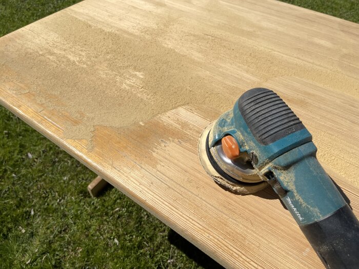 En slipmaskin använd på en bordsskiva av trä med repor och gammalt klarlack som håller på att slipas bort.