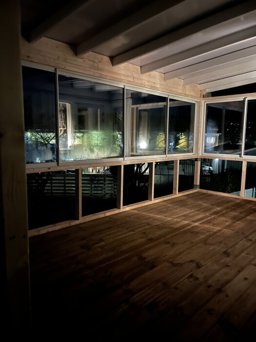 Inglasad balkong med skjutbara fönster och träpanel, under konstruktion på natten.