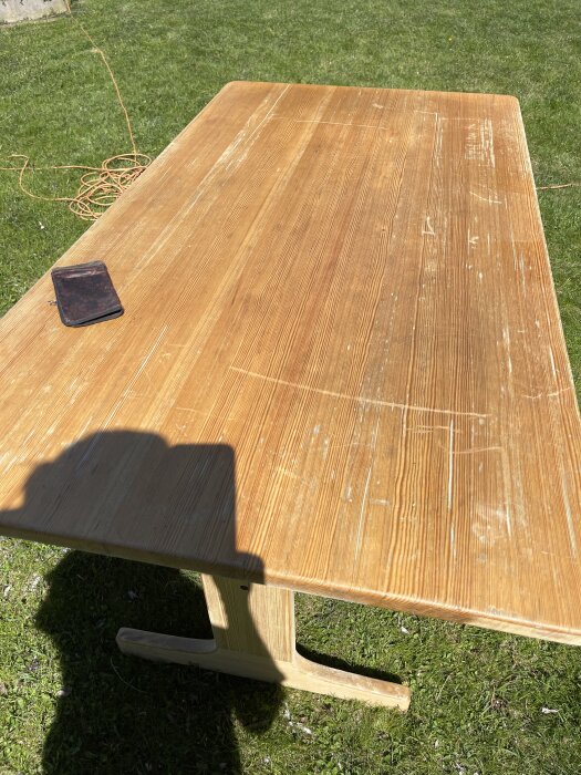 Slitet träbord på gräsmatta i solljus, skugga av person och mobil ovanpå.