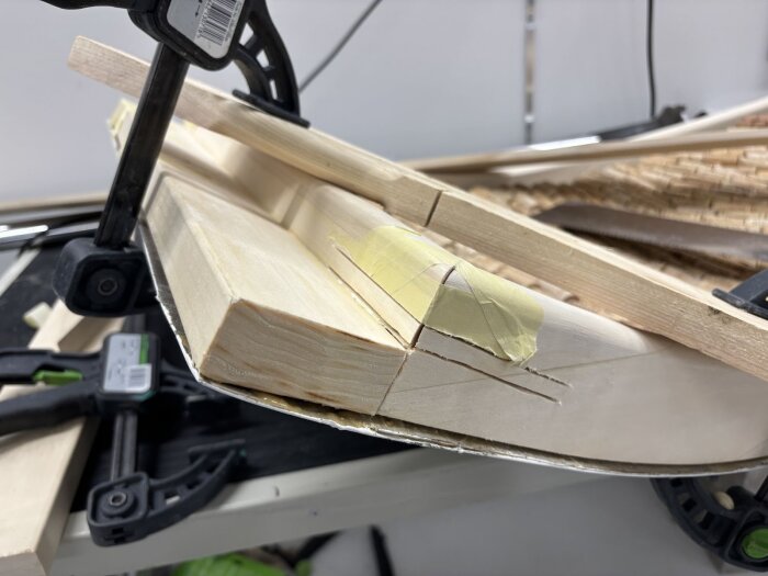 Träbit limmad och hålls ihop av klämma, provisoriskt uppsatt med tejp. Möjligen del av en dörrkarm i ett renoveringsprojekt.