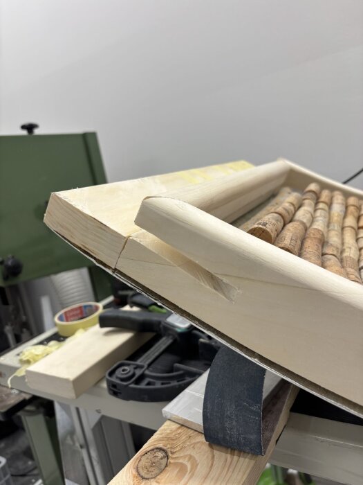 Träbit med urfräst urtag sett snett uppifrån på arbetsbänk, omgiven av verktyg och korkar i bakgrunden.