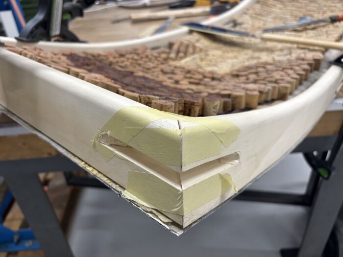 Hörn av dörrkarm i trä med tejpad träfog, korkbitar fästa ovanpå, ligger på en arbetsbänk.