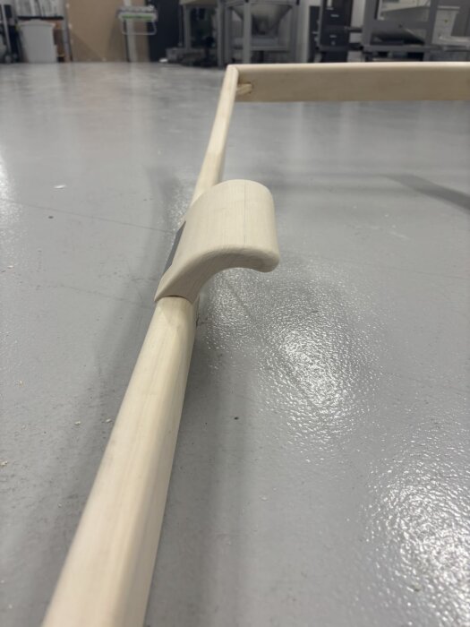 Träram med ett nyligen tillverkat trähandtag placerat på golvet, del av ett pågående byggprojekt i verkstadsmiljö.