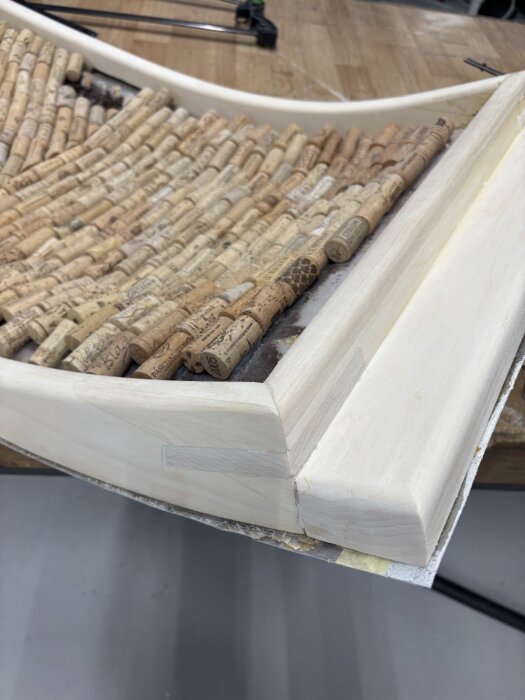 Träram med sågade hörn och korkfyllning synlig ovanpå, del av ett dörrkarmprojekt i konstruktion.