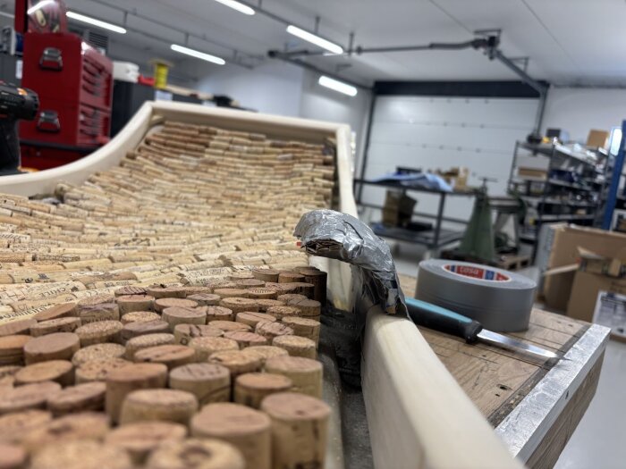 En dörrkarm täckt med vinkorkar under konstruktion i verkstadsmiljö, med verktyg och tejp synliga.