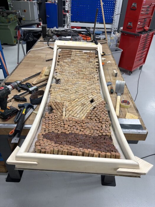 Träram på arbetsbänk med många vinklar och korkar inuti, verktyg runtomkring i verkstadsmiljö.