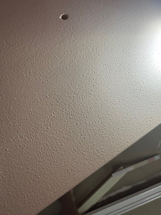 Målad yta på en bokhylla med ojämn finish, synliga prickar och kratrar, troligtvis orsakade av luftbubblor vid användning av skumroller.