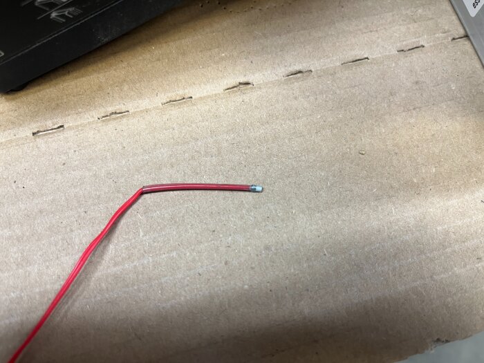 Röd kabel med en PTC-sensor i änden ligger på en kartongyta, med en del av en maskin synlig i bakgrunden.