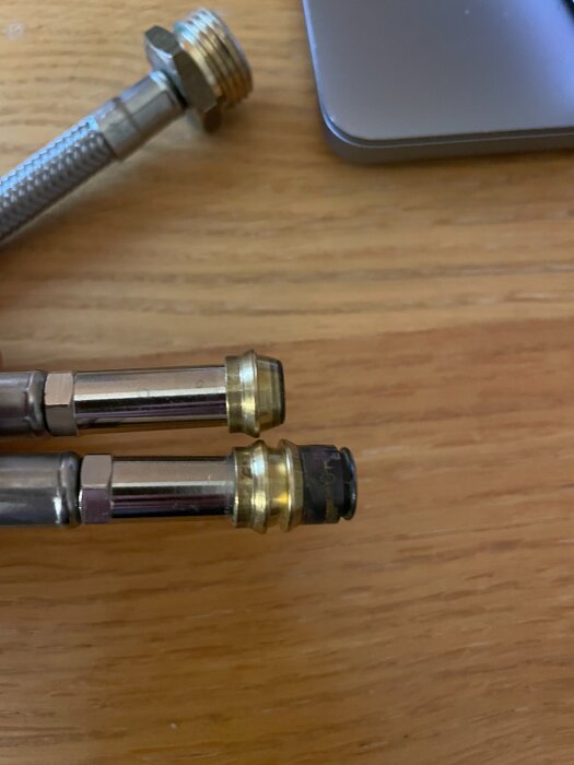 Två blandarrör med olika klämkopplingar, ena med svart del, liggande på träbord; osäkerhet kring övergång från 10mm till 12mm kopplingar.