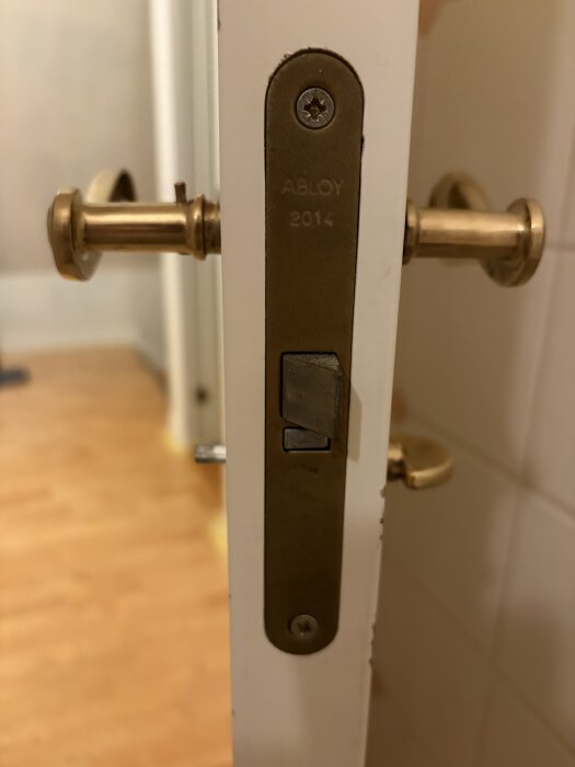 Äldre dörrvred utan skruv på en vit toalettdörr, med texten "ABLOY 2014" synlig på låset.