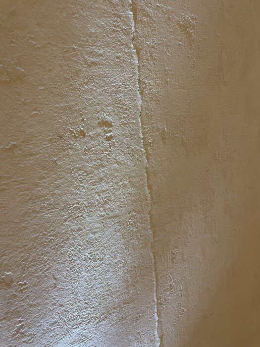 Strukturtapet i ett vardagsrum med en tydlig reva längs en murstock.