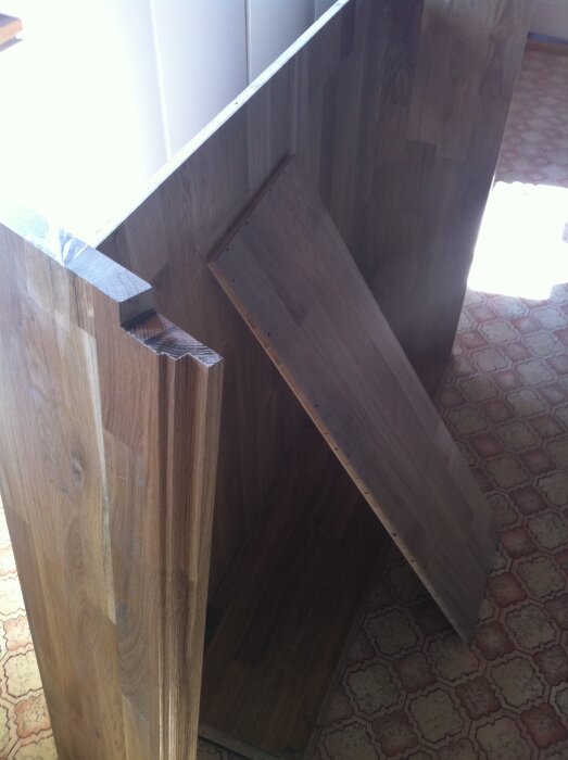 Träpanelskivor i ett rum med mönstrat golv, en skiva lutande mot väggen och markerade urtag synliga.