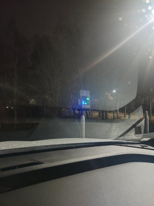 Bilens instrumentbräda sedd inifrån bilen; exteriör belysning och laddstation synlig i mörker utanför fönstret.