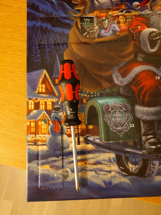 Skruvmejsel placerad på en julkalender med vinterlandskap och jultomtens släde.