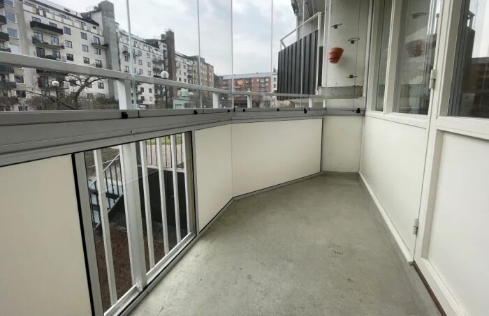Inglasad balkong med glasväggar och utsikt över bostadshus.