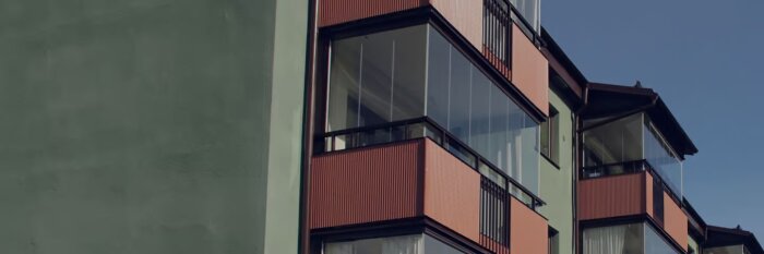 Flerfamiljshus med inglasade balkonger och röda balkongräcken.