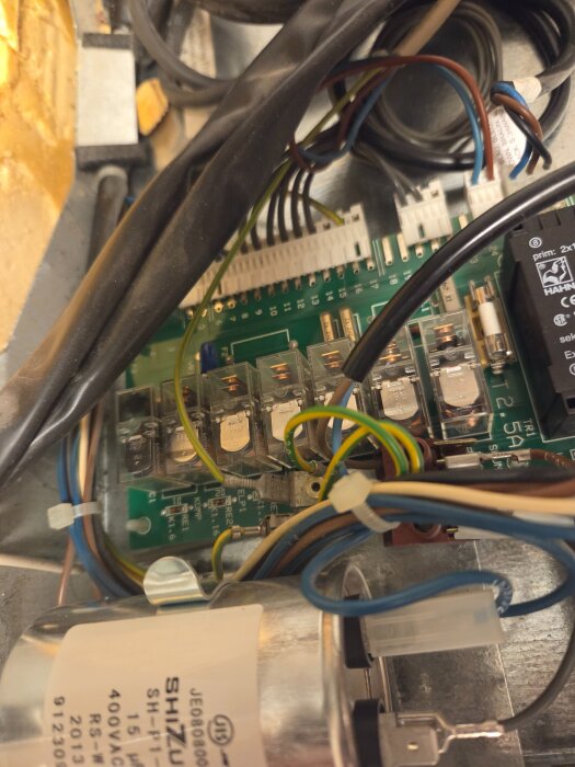 Elektrisk kretskort med kablage och komponenter, inklusive reläer och kondensator med märkningen Shizuki, insidan av en maskin eller apparat.