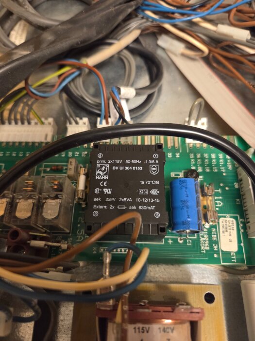 Elektronisk krets med transformator, kondensator och flera kablar på ett kretskort.