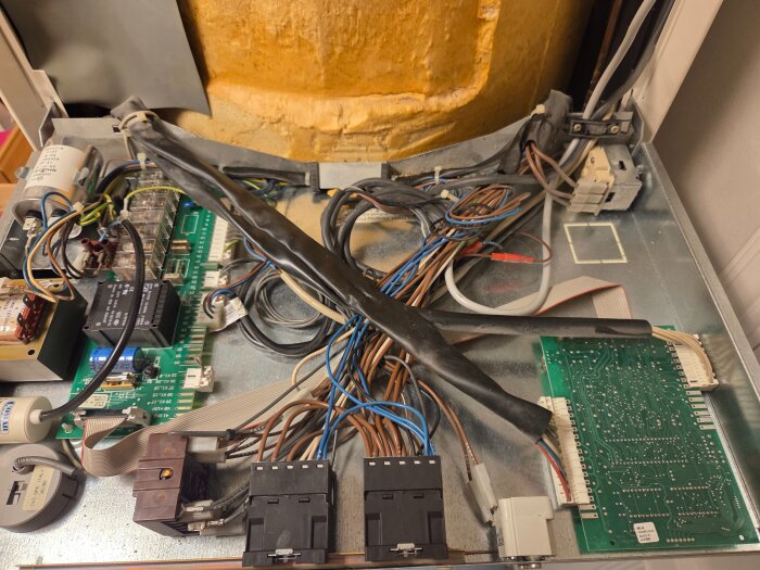 Elektroniska kretskort och kablar inuti en apparat, med isolering synlig i bakgrunden och flera anslutningar.