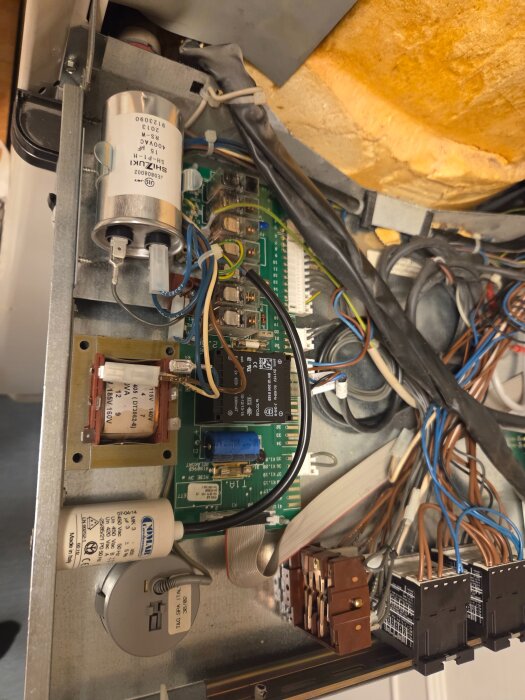 Kretskort med diverse elektriska komponenter och sladdar inuti en apparat, inklusive kondensatorer och kopplingskablar.