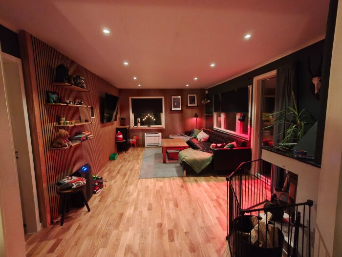 Renoverat vardagsrum med nya väggpaneler och infällda högtalare, träbord och soffa, dolda kablar, och installerad belysning i taket.