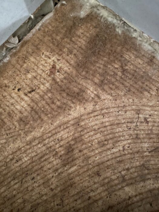 Gammal plastmatta från 70-talshus under renovering, visar ytskikt med möjligen asbest- eller limrester.