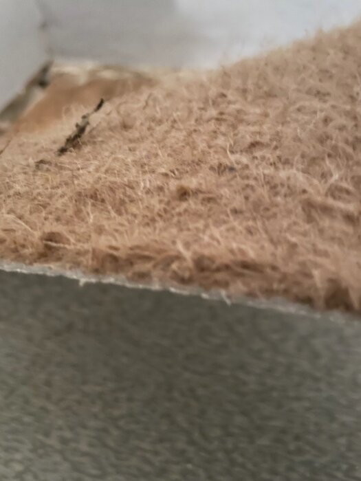 Närbild av borttagna golvskikt från en plastmatta, med fokus på ytrandets textur och färg, för att bedöma potentiell asbest.