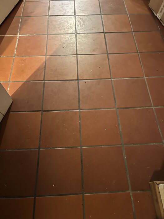 Orange klinkergolv med slitna fogar i en källare. Golvvärme under keramiska plattor, några plattor är lösa och fogen saknas delvis.