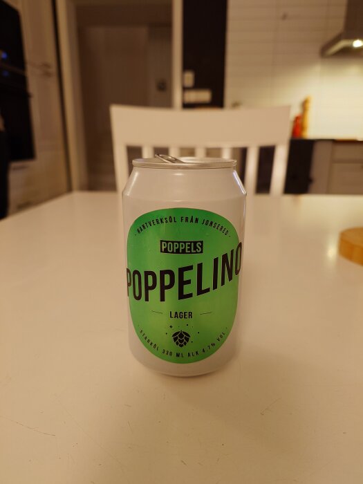 En burk Poppelino lageröl står på ett köksbord framför en vit stol i ett kök.