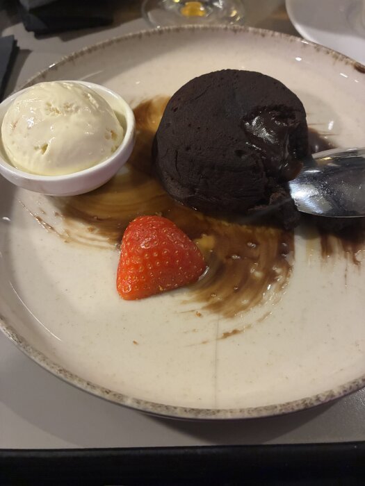En tallrik med chokladfondant, serverad med en skopa vaniljglass och en jordgubbe.