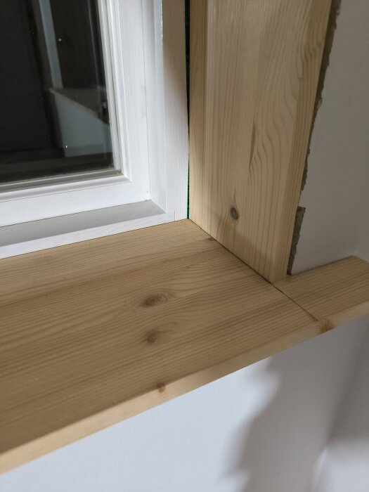 Fönstersmyg i trä där fönsterbrädan inte når hela vägen till fönsterkarmen, synlig skillnad i design mot äldre husdel.