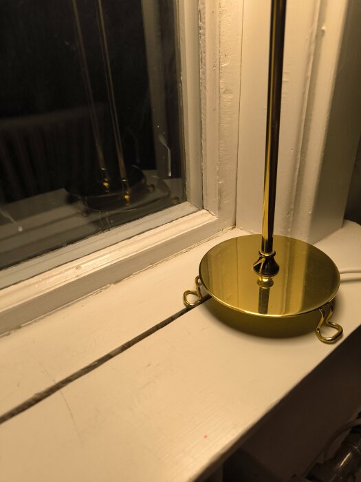 En vit fönsterbräda med en guldfärgad lampa nära fönstret, där brädan inte livar med fönstrets karmkant.