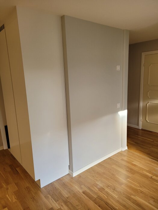 Grå vägg mot vit högskåp i ett rum med trägolv, med fokus på området där fog behövs för att hantera rörelse.