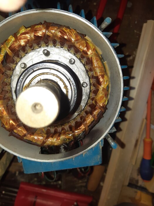 Närbild av en demonterad elmotor med synliga kopparlindningar och centralt placerad axel. Spår av hantering syns på komponenterna.