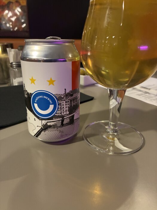 En burk Nyköping Brewing - Birramisu och ett glas öl står på ett bord, bakgrund av pubmiljö.