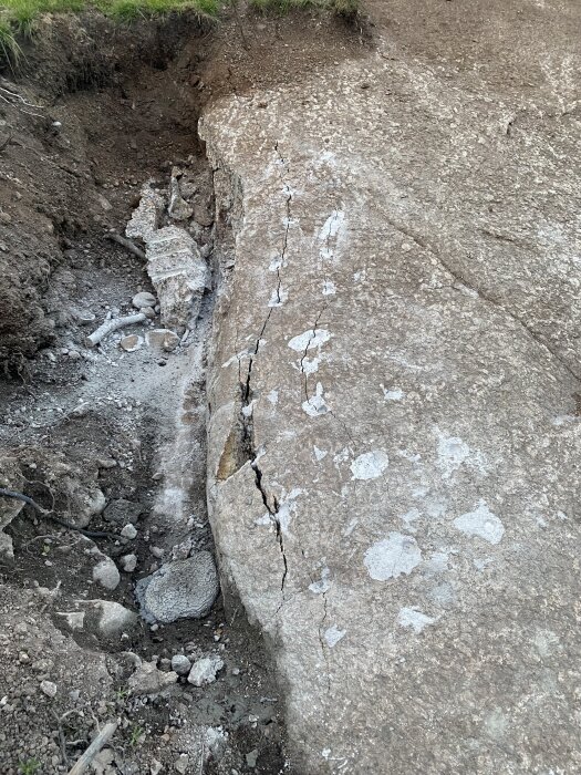 Berg med sprickor efter användning av snigeldynamit för spräckning, omgiven av grus och jord vid kanten av en grävd yta.