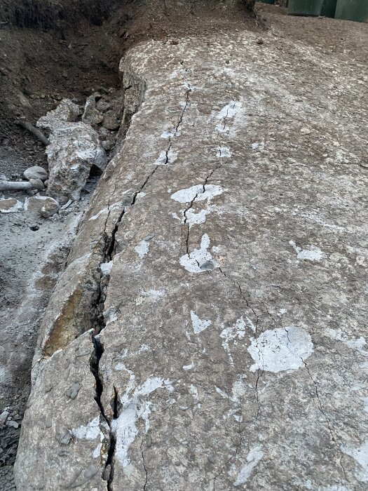 Sprickor i en bergyta efter användning av snigeldynamit, med synliga borrhål och skarpa kanter längs en rak linje i terrängen.