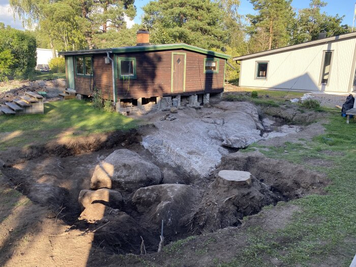 Välgrävd tomt med stora stenar och stubbe nära hus. Förbereder för att flytta poolen och undvika mer bergarbete.