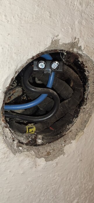 Elektrisk kopplingsdosa i vägg med blå och svart elkabel ansluten till sockerbit.