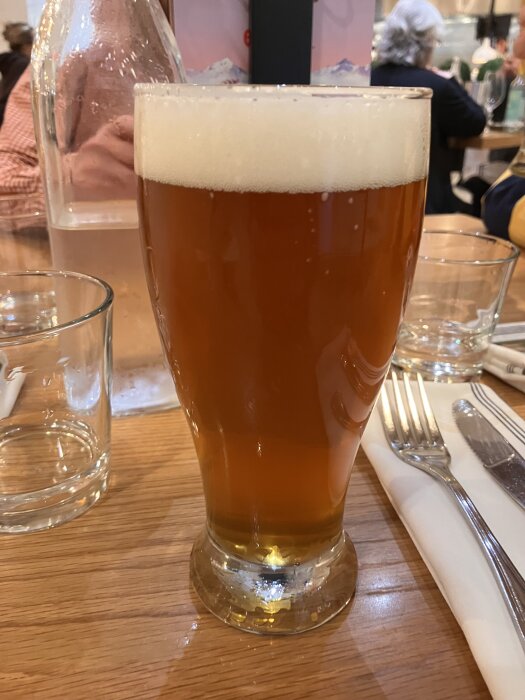 Ett glas med Cigar City IPA, ett bärnstensfärgat öl med skumkrona, står på ett träbord bredvid bestick och ett glas.