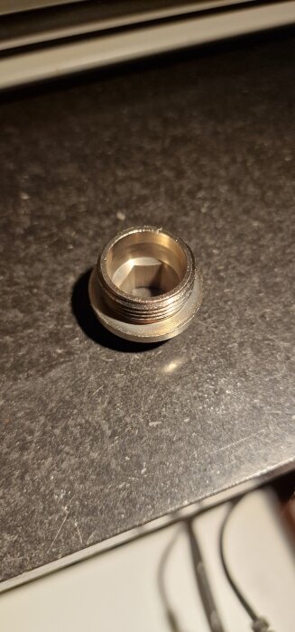 Metallnippel med gängad yta på mörk yta, använd för anslutning av vinkelkopplingar till radiatorer med M22 mått.