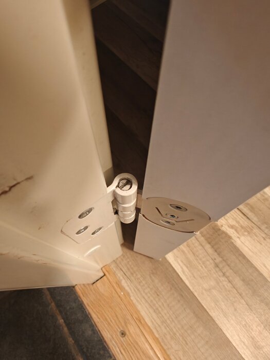 Närbild av ett gångjärn på en innedörr, med synliga justeringsskruvar. Problemen uppstår när dörren inte stannar öppen.