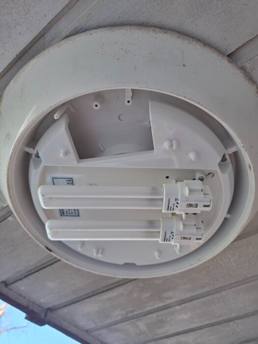 Rund taklampa med två lysrörsarmaturer monterad på ett innertak av trä.