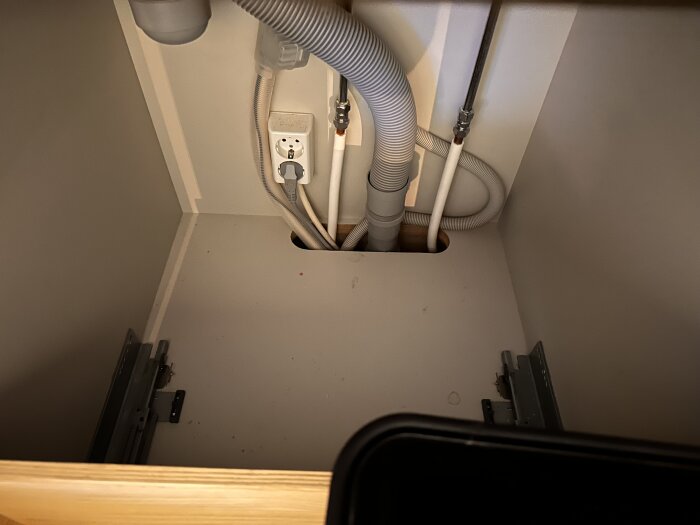 Avlångt hål under diskbänk med rör och eluttag synliga, behov av droppskydd eller tätning.