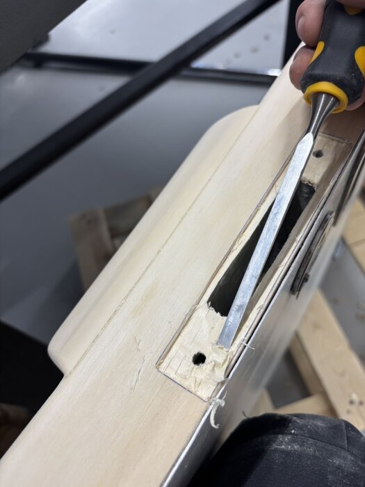 En dörrkarm där en person använder en stämjärn för att justera en urfräsning för montering av låskista.