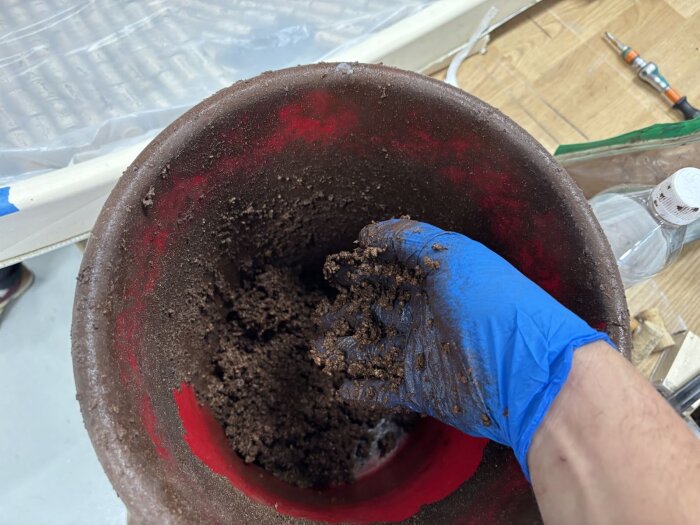 Blåhandskad hand blandar brun massa i en röd balja. Arbetet ser ut att ingå i processen att fylla ut och jämna till runt en dörrkarm.