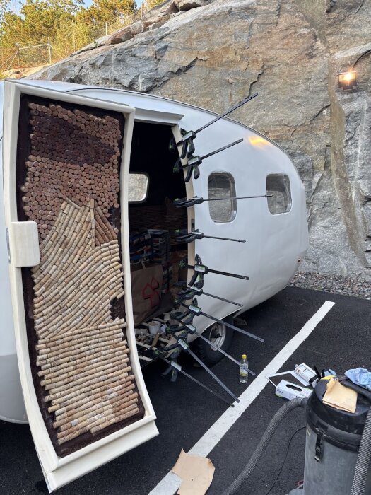 Dörr med korkar och tvingar fästa på en husvagn under renovering, omgiven av verktyg och berg i bakgrunden.