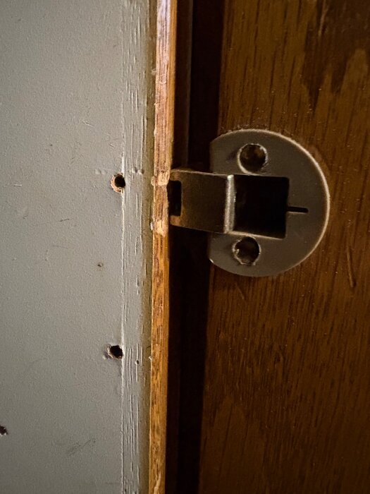 Närbild på ett dörrlås monterat på en träram, med borrhål synliga i träpanelen bredvid.