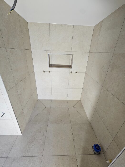 Modernt badrum med stora släta plattor och korrekt golvfall mot väggavloppet. Inget hinder för tårna, redo för duschinstallation.